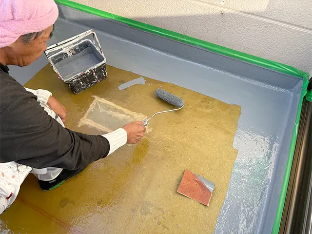 ベランダの床面と、壁際の立ち上がり部分の防水改修を行いました。
ガラス繊維のマットに樹脂を含ませて防水層をつくり、雨水の浸入を防ぎます。
壁との境目や排水口の周辺など、細かな部分までていねいに施工。
グレーの保護塗装で仕上げ、傷みが目立っていた床を、すっきりとした印象に整えました。